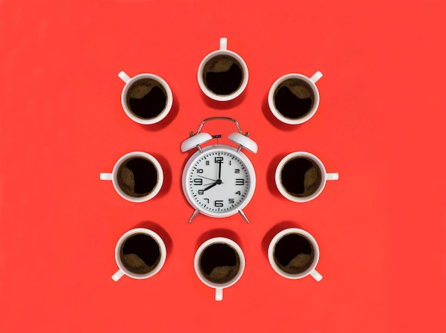 White alarm clock and coffee cups on the red background Top view Copy space