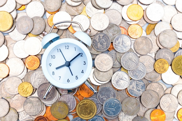 white alarm clock on golden and silver coins.