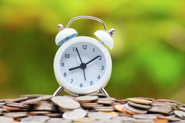 white alarm clock on golden and silver coins.