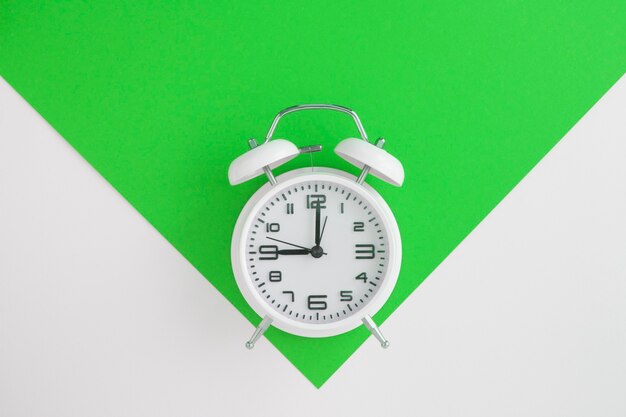 White alarm clock on the green and white background. Top view. Copy space. Location vertical.