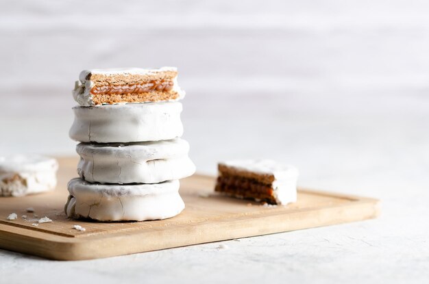 White alfajores filled with dulce de leche on a wooden board and white background.