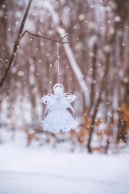 A white angel made of macrame hangs on a branch in a snowy forest The symbol of Christmas