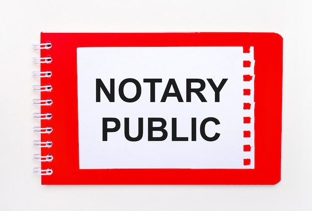 On a white background - a bright red notebook on a spiral. On it is a white sheet of paper with the text NOTARY PUBLIC