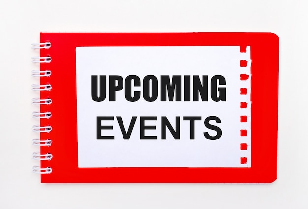 On a white background - a bright red notebook on a spiral. On it is a white sheet of paper with the text UPCOMING EVENTS