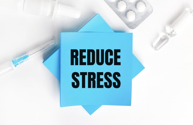 On a white background, a syringe, ampoule, pills, a vial of medicine and light blue stickers with the inscription REDUCE STRESS. Medical concept