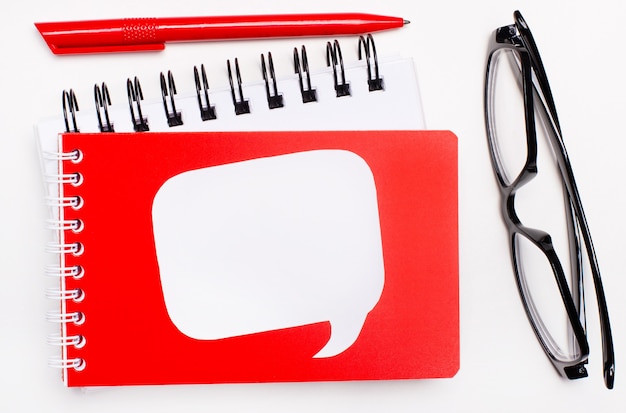 On a white background, white and red notepads, black glasses, a red pen and a white blank card with a place to insert text.