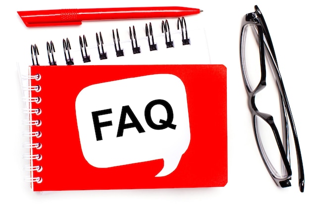 On a white background white and red notepads black glasses a red pen and a white card with the text FAQ