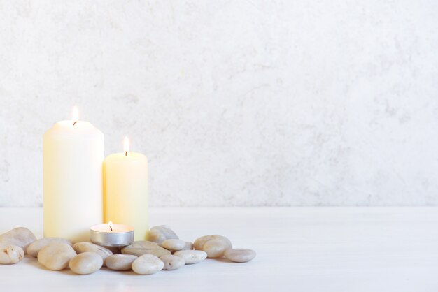 Photo white background with three burning candles and stones