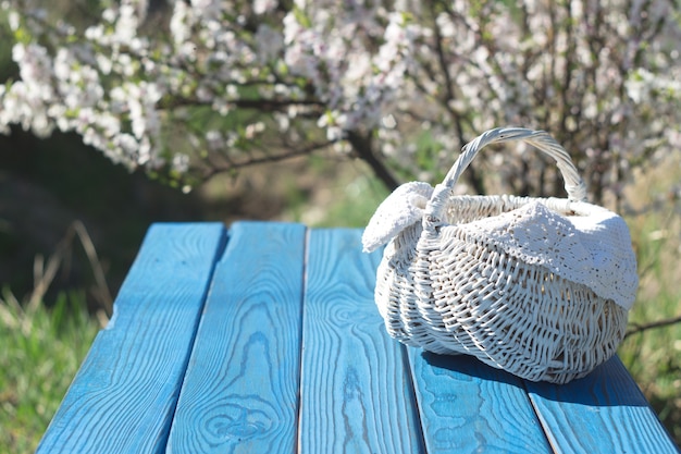 White basket on a table of blue boards against the background of a flowering bush