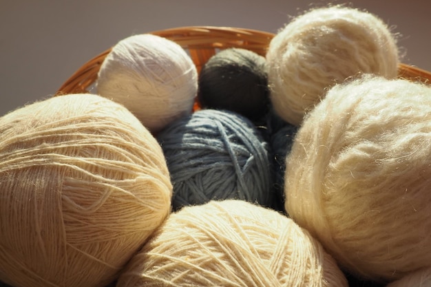 White beige and blue woolen and acrylic threads wound into a ball or skein Several skeins of light yarn in a basket Knitting as a hobby A clew of thread