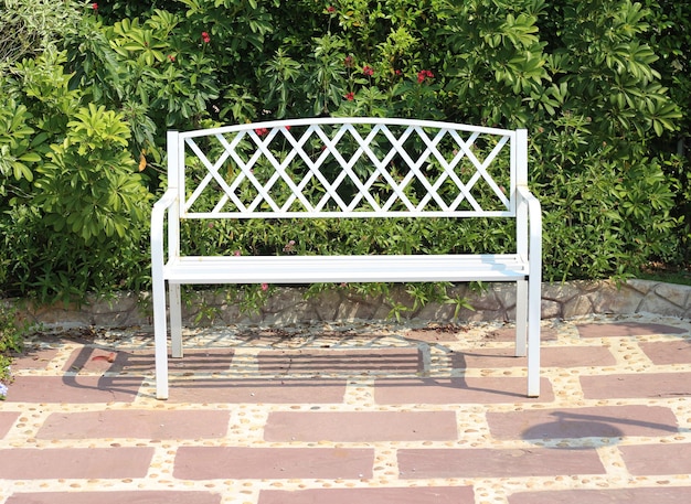 white bench is sitting on a brick walkway next to a bush