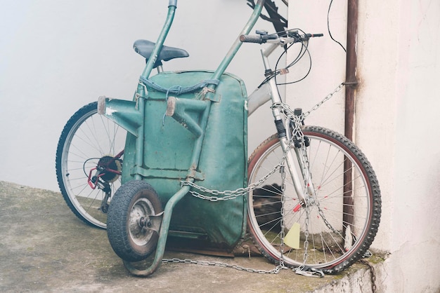 White bike and green wheelbarrow near a white wall on the chain Toned