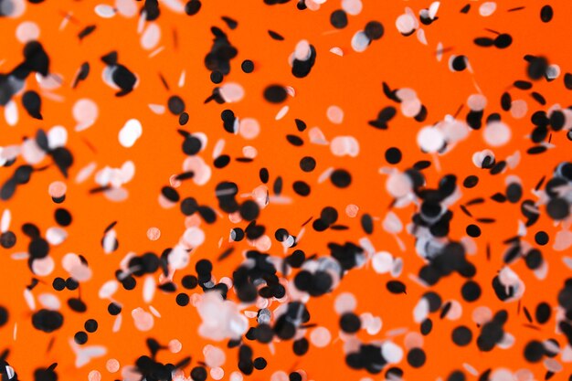 White black confetti flying on orange background halloween party