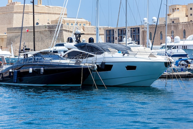 White and black modern motor yachts are moored in port on the cityscape background.