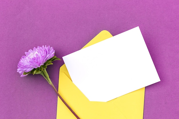 White blank card yellow envelope and flower on purple background Minimal style Top view Flat lay Mockup