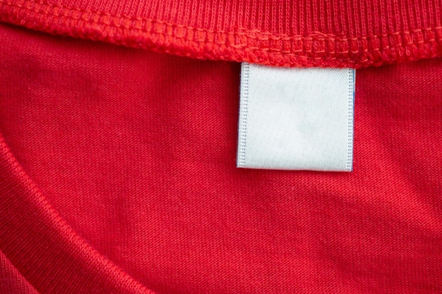 White blank clothing tag label on new red cotton shirt fabric texture background