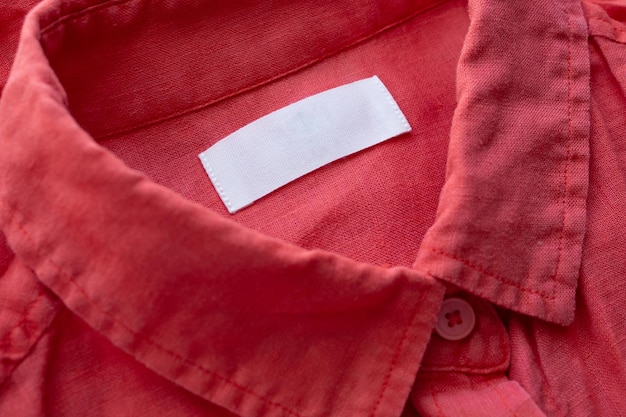 White blank clothing tag label on red linen shirt fabric texture background