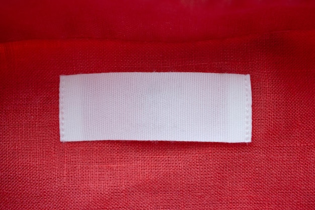 White blank clothing tag label on red linen shirt fabric texture background