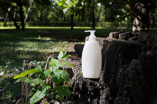 White blank cosmetic bottle with cream, moisturizing lotion or shampoo on wood background with green leaves. Natural Organic Spa Cosmetic Beauty Concept. Mockup