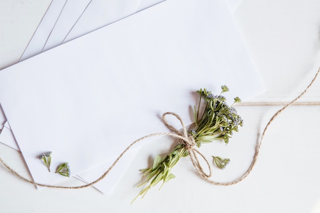 A white blank envelopes with a small bouquet of wildflowers tied with twine on a white wooden surface