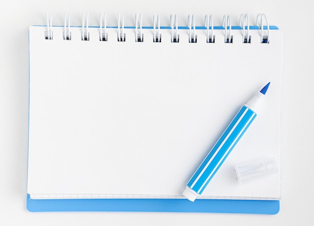 White blank notebook and blue marker on white. Top view, mockup.