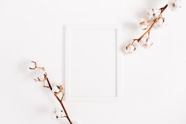 White blank photo frame mock up and cotton branches. Flat lay, top view