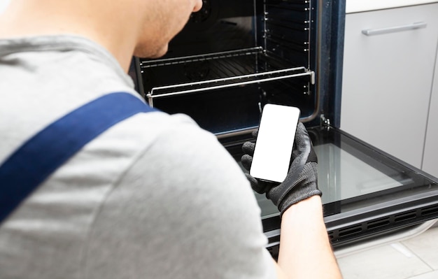 White blank screen on phone in repairman hand who has come to repair the oven Smartphone mockup with empty space Place for text on phone screen