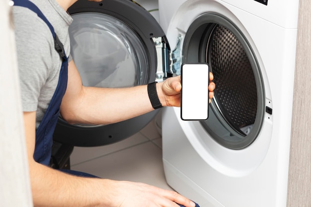 White blank screen on phone in repairman hand who has come to repair the washing machine Smartphone mockup with empty space Place for text on phone screen