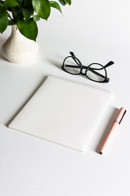 A white blank spiral notebook with a pen is lying on a white table