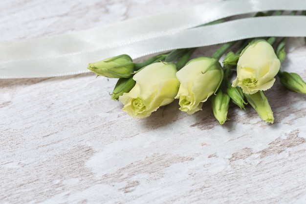 White blooming rose buds on wooden table with copy space. Tender roses and ribbon.