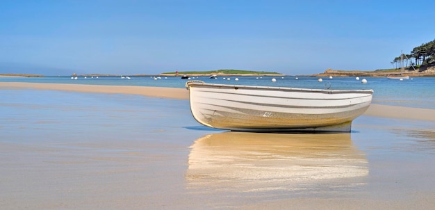 White boat placed on the sand near the blue sea with reflection on the wet sand