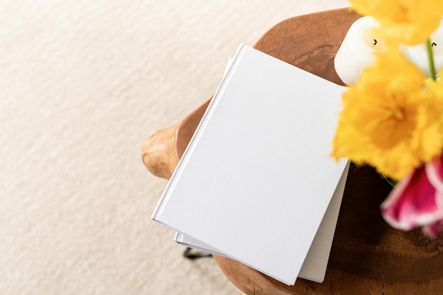 White book blank cover mockup on stylish wooden coffee table with tulips bouquet high angle view