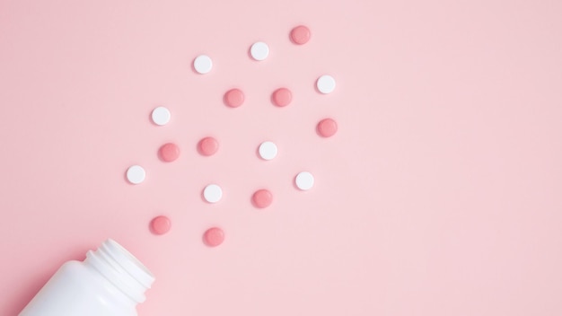 White bottle container with medication tablets on pink background Concept of healthcare and medicine