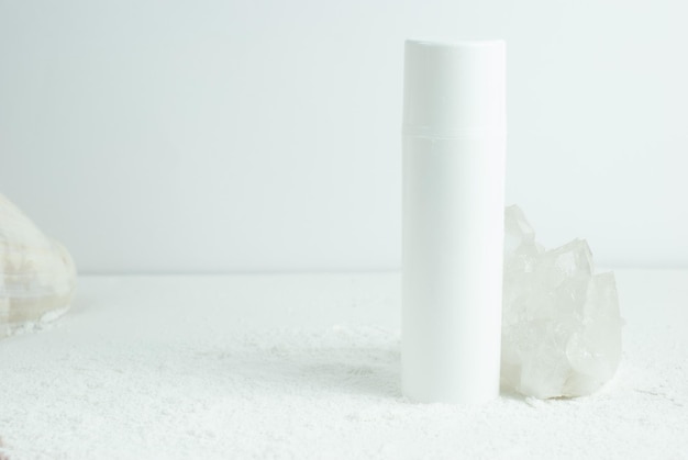 A white bottle of lip balm sits in a pile of white rocks.