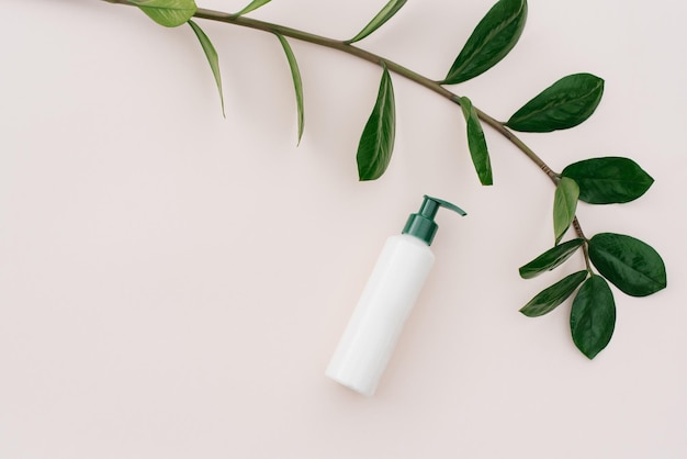 White bottle with a dispenser and tropical green leaves on a beige background