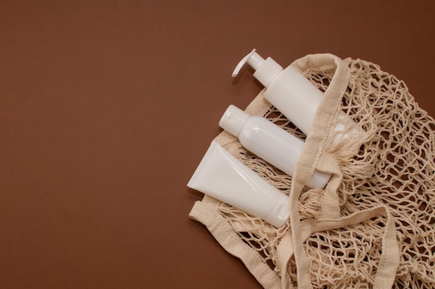 White bottles with cosmetics on a brown background and a string bag in a vertical format