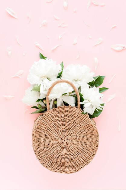 White bouquet of peonies in a straw bag on pink background minimal floral concept greeting card flat