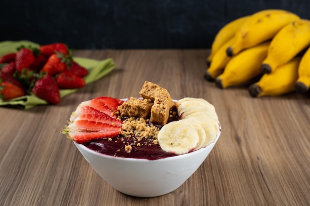 White Bowl of Brazilian Frozen Acai Berry With Pacoca, Strawberry and Banana. on a wooden desk