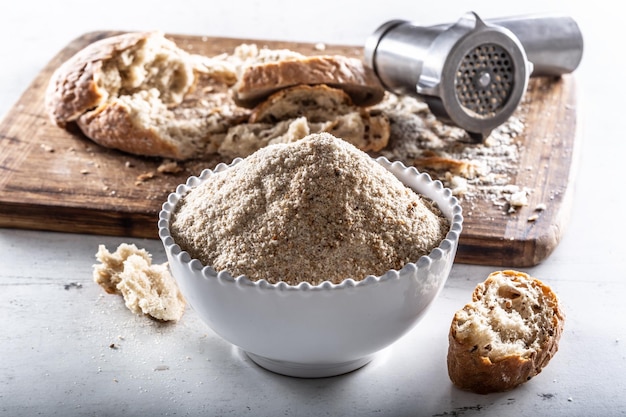 A white bowl full of breadcrumbs and old dry bread around