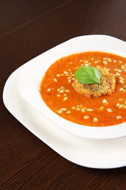 a white bowl full of fresh vegetable cream soup with pine nuts and piece of toast with basil