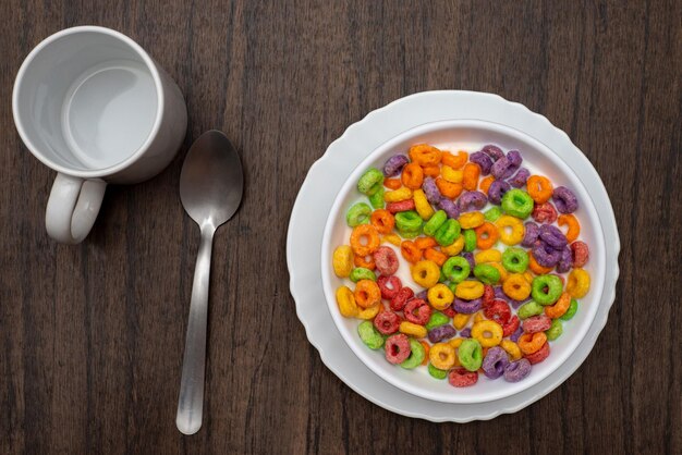 White bowl with cereal in the form of colored rings on wooden table Cereal breakfast