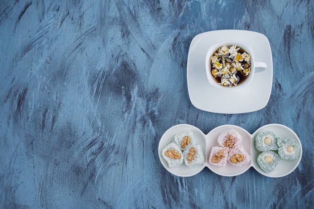 White bowls of various sweet delights with nuts and tea on blue surface. 