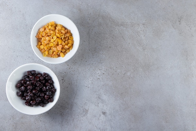 White bowls with dried golden raisins on stone surface