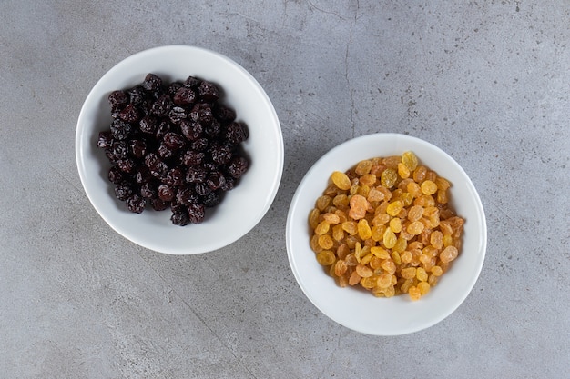 Photo white bowls with dried golden raisins on stone surface.