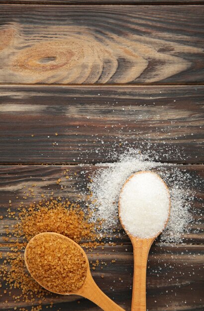 White and brown sugar in spoon on brown background