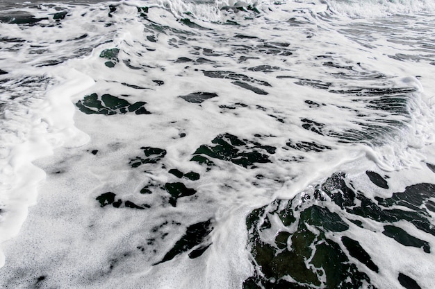 White bubbles of wave crash the sandy beach