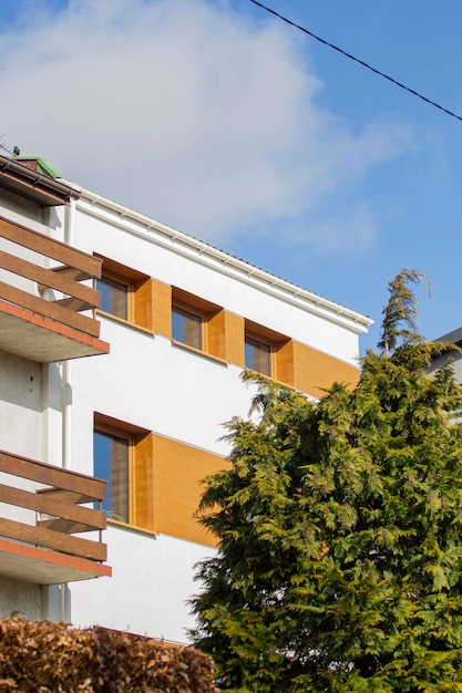 A white building with a balcony and a tree in front of it.