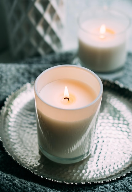 White burning candle in glass candleholder on vintage metal tray warm cozy home