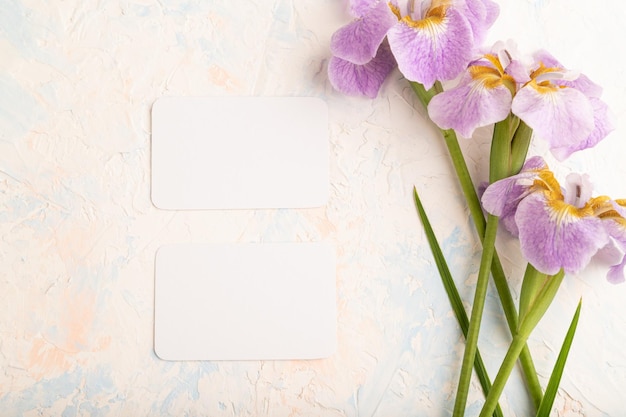 White business card with lilac iris flowers on white concrete background top view copy space