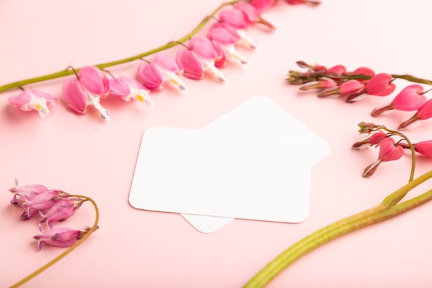 white business card with pink dicentra, broken heart flowers on pink pastel background. side view